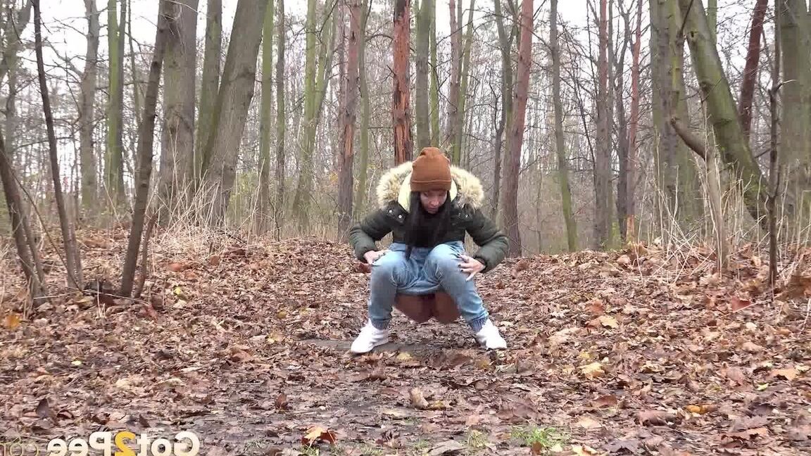 15P Dark-haired girl squats for a pee on leaf covered ground on a chilly day