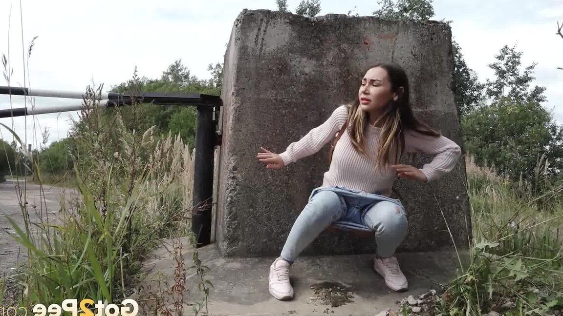 15P 服を着た女の子サーシャが小道のコンクリートブロックの後ろでしゃがんで小便をする