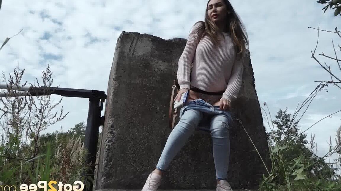 15P 服を着た女の子サーシャが小道のコンクリートブロックの後ろでしゃがんで小便をする