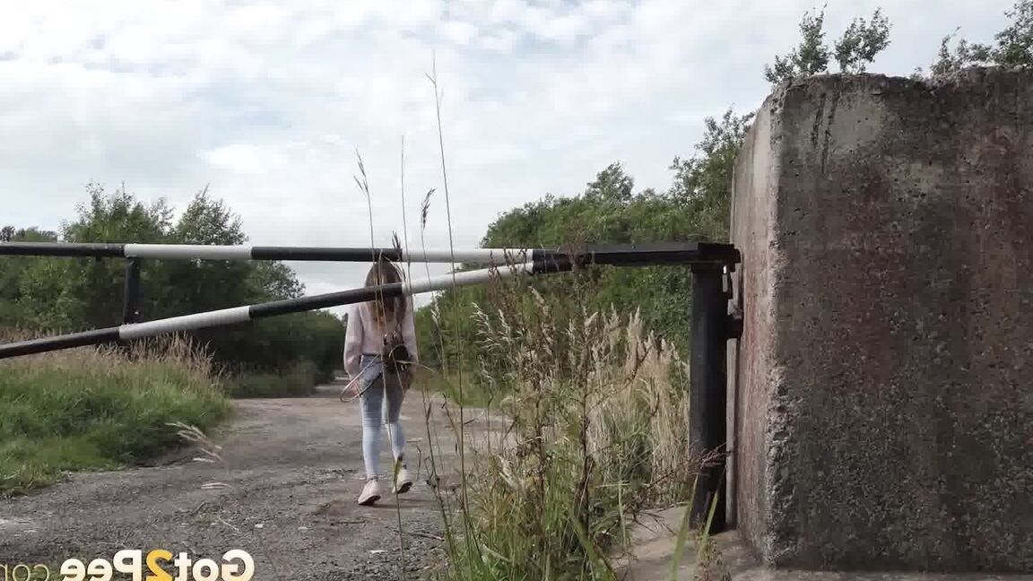 15P 服を着た女の子サーシャが小道のコンクリートブロックの後ろでしゃがんで小便をする