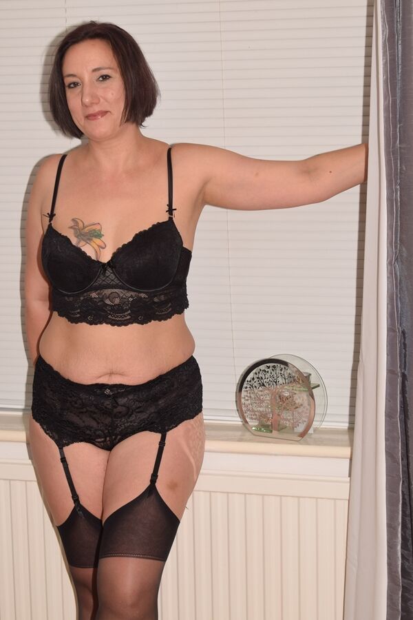 20P Une femme plus âgée en lingerie noire trois pièces et bas de nylon expose ses petits seins