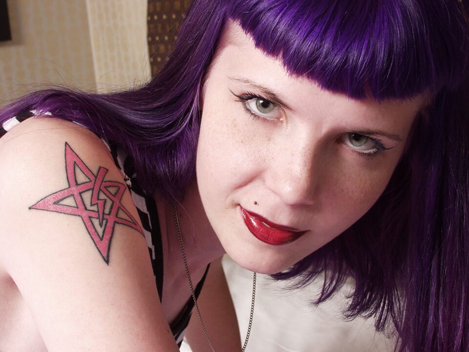 Das 16P-Gothic-Girl Szandora macht sich völlig nackt auf einem Bett aus und trägt dabei lila Haare