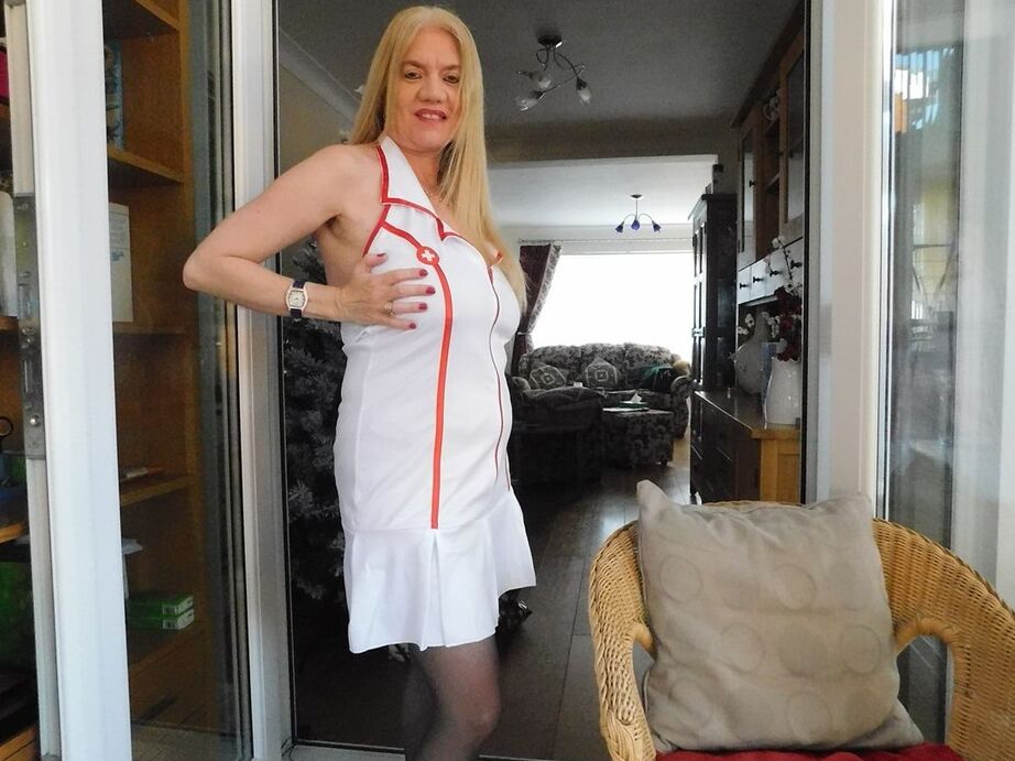 20P Older British nurse Lily May unzips her uniform on a wicker chair