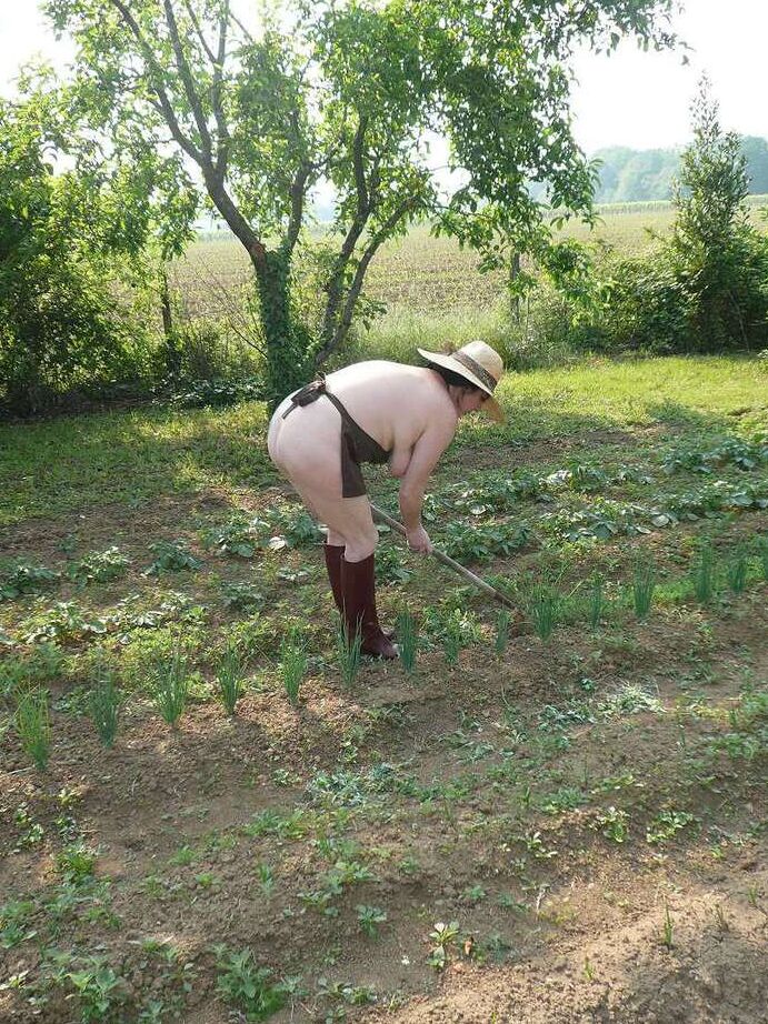 20P La señora madura Mary Bitch cuida su jardín desnuda con sombrero y delantal