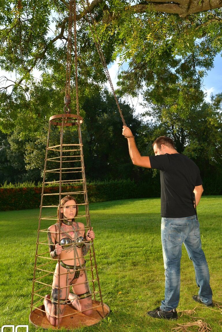 Lauren, soumise et encrée de 21P, pose dans une cage extérieure alors qu'elle est enchaînée.