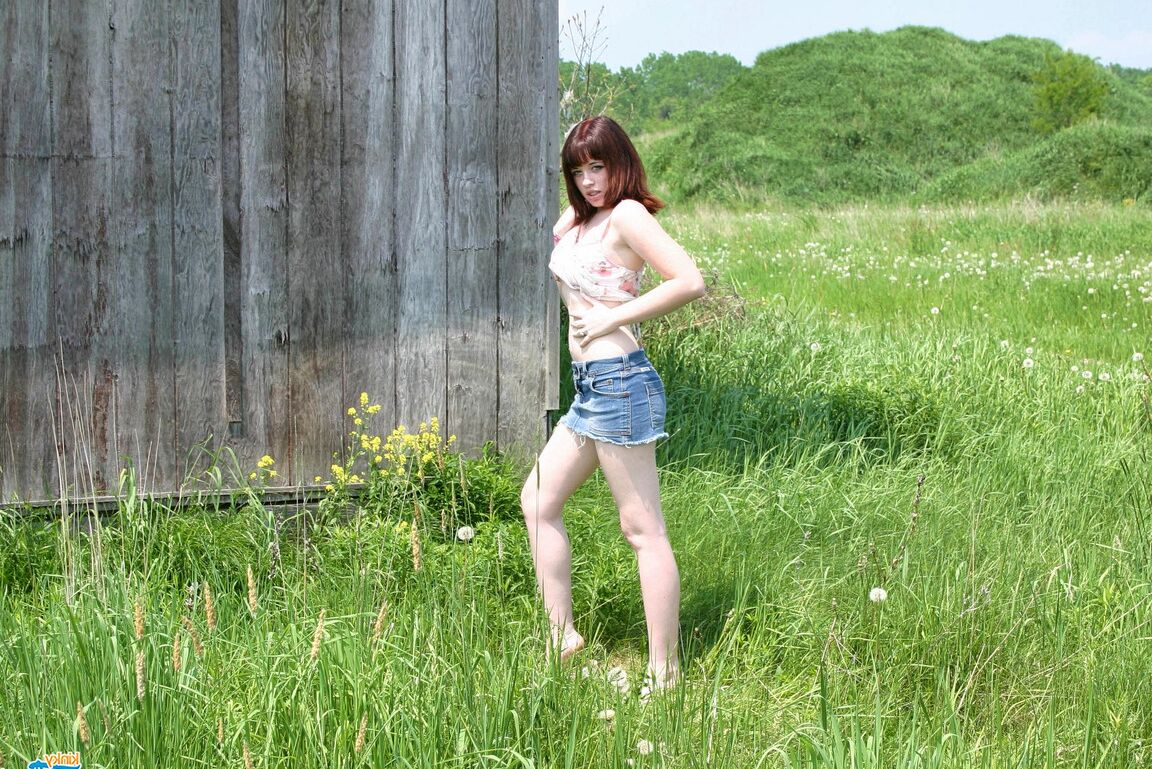 12P Young redhead Barbie A exposes her breasts against a building in a field