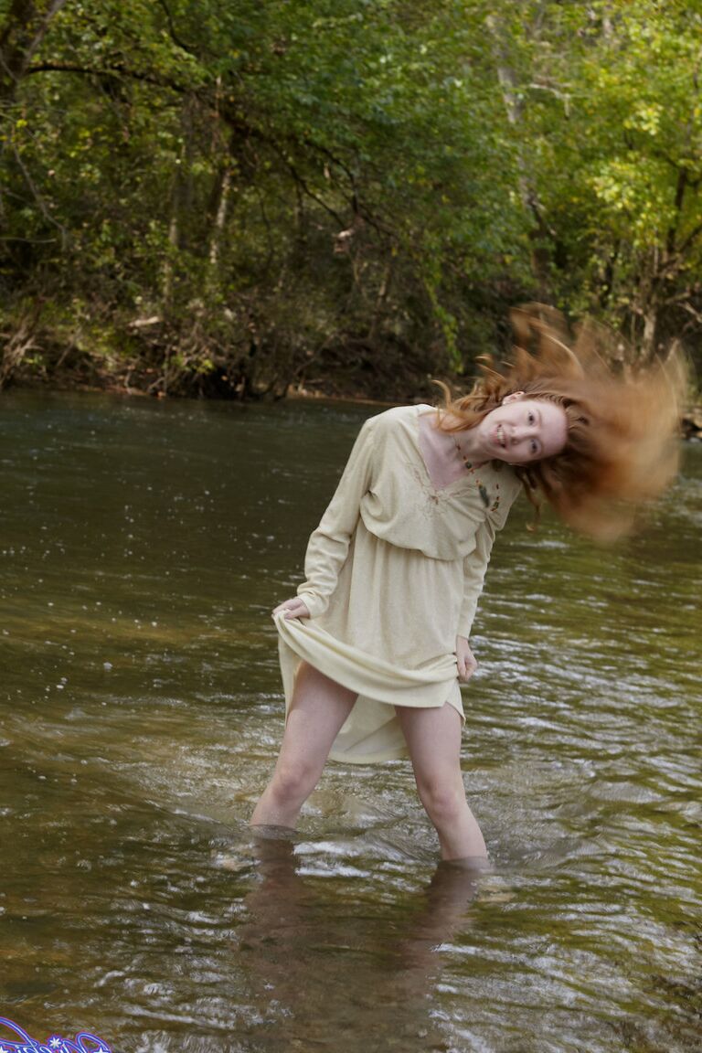 15P Natural redhead Nicki Blue shows some leg while wading into a shallow stream