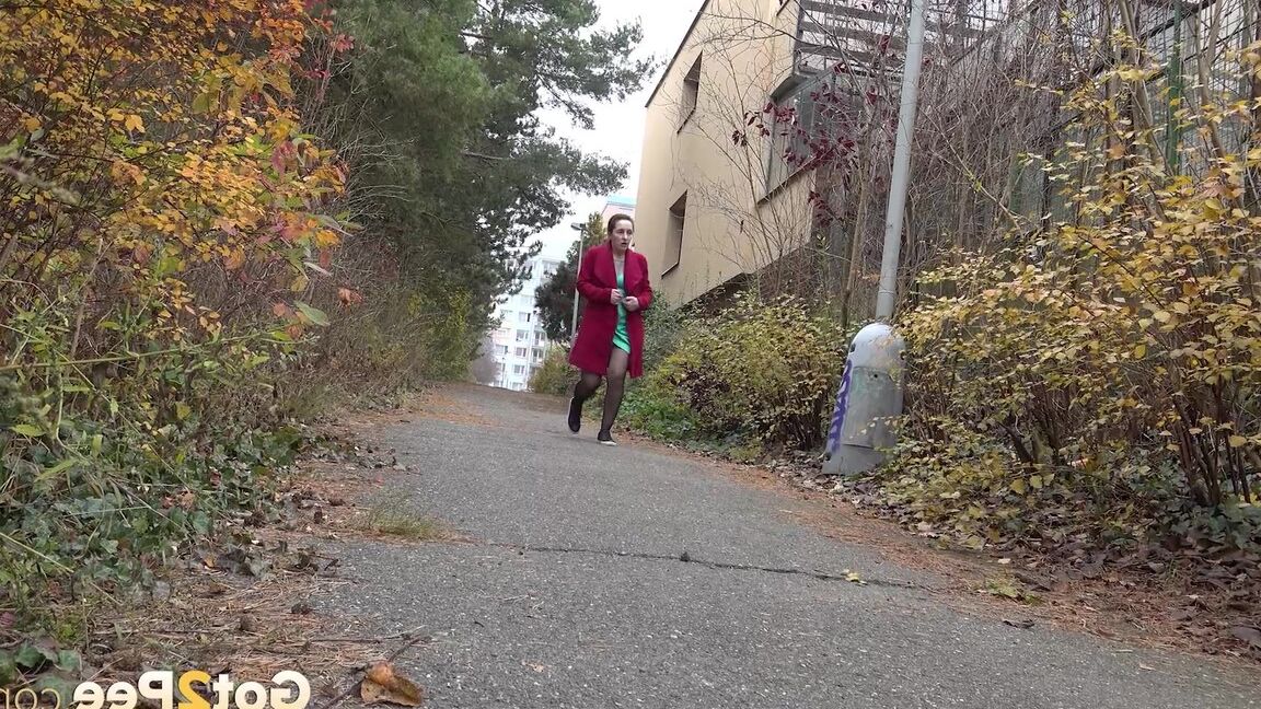 15P Caucasian female Lora takes a piss while walking on a pathway in the city