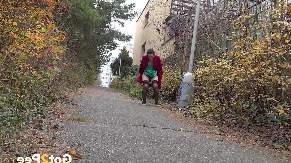 15P Caucasian female Lora takes a piss while walking on a pathway in the city
