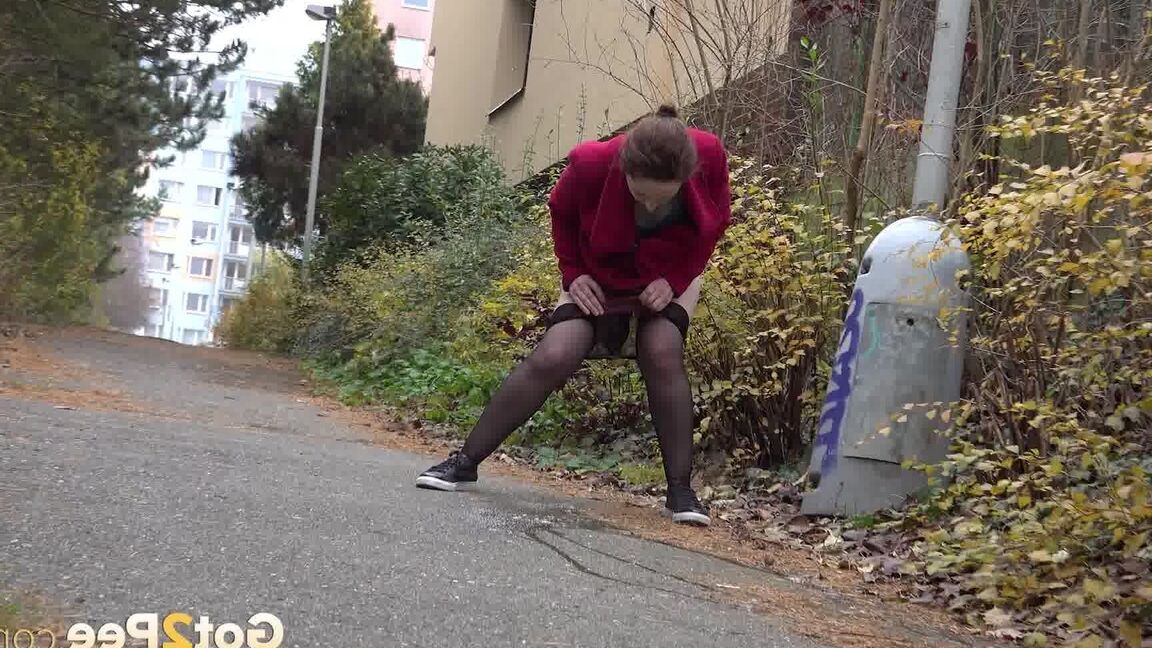 15P Caucasian female Lora takes a piss while walking on a pathway in the city