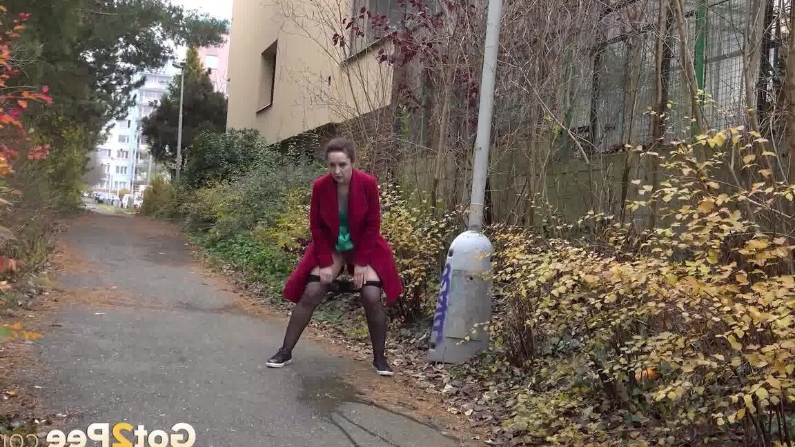15P Caucasian female Lora takes a piss while walking on a pathway in the city