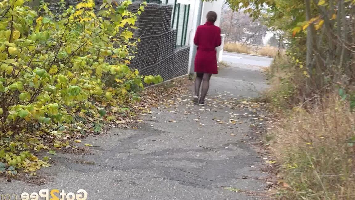 15P Caucasian female Lora takes a piss while walking on a pathway in the city