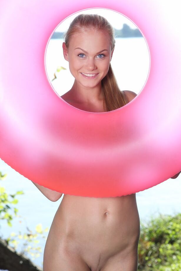 18P La joven rubia desnuda Nancy A posa sola en una cámara de aire rosa junto al agua