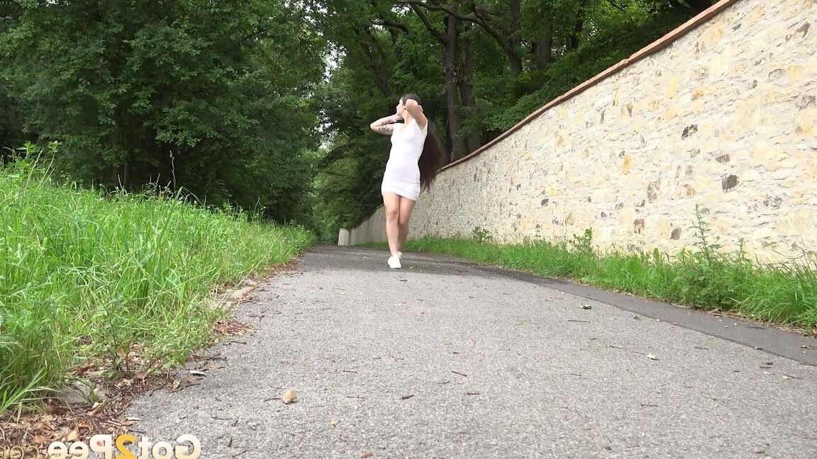 15P Die kaukasische Frau Lara Fox zieht ihr Kleid hoch, um auf einem gepflasterten Gehweg zu pinkeln