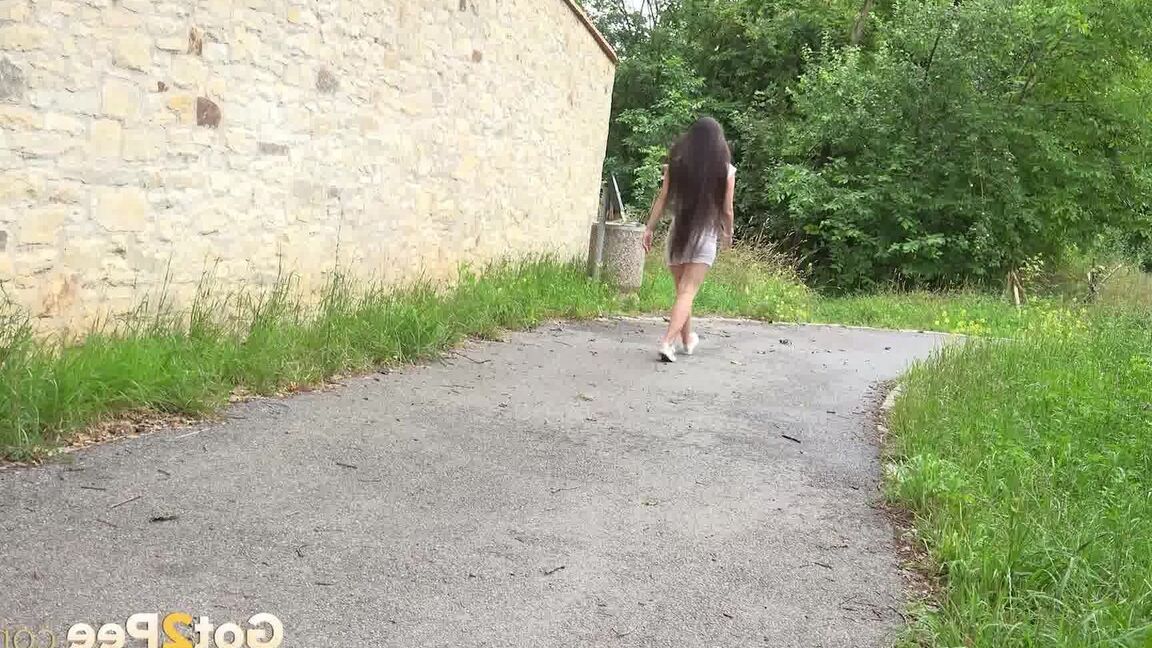 15P Die kaukasische Frau Lara Fox zieht ihr Kleid hoch, um auf einem gepflasterten Gehweg zu pinkeln