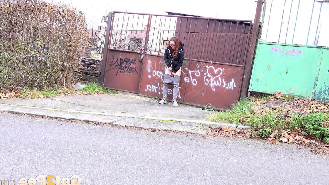 15P Redheaded girl pulls down her pants to take a piss in front of steel gates