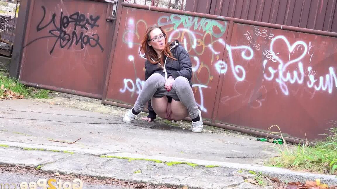 15P Redheaded girl pulls down her pants to take a piss in front of steel gates