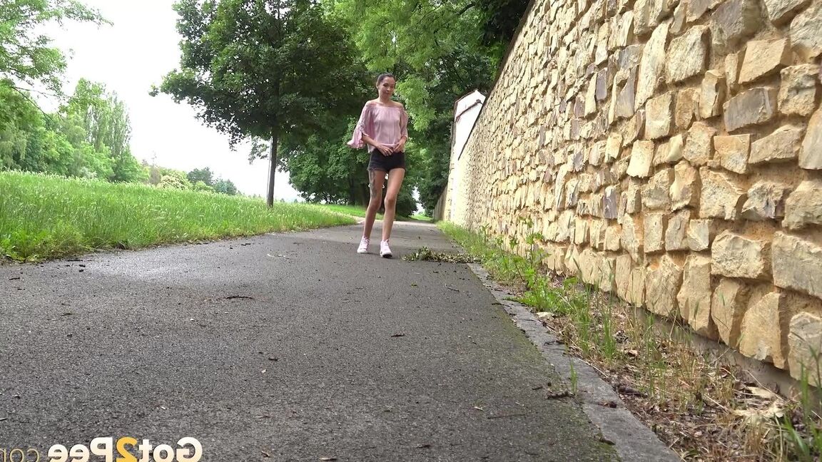 15P Short taken girl Mistica squats for a piss on a paved path in an urban setting