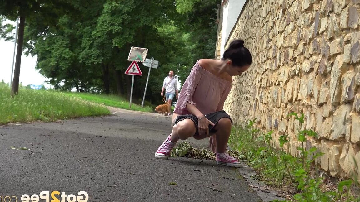 15P Short taken girl Mistica squats for a piss on a paved path in an urban setting
