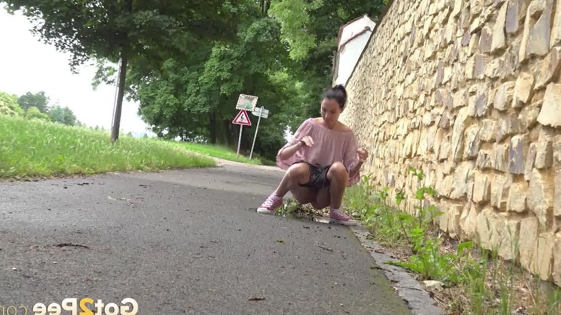 15P Short taken girl Mistica squats for a piss on a paved path in an urban setting