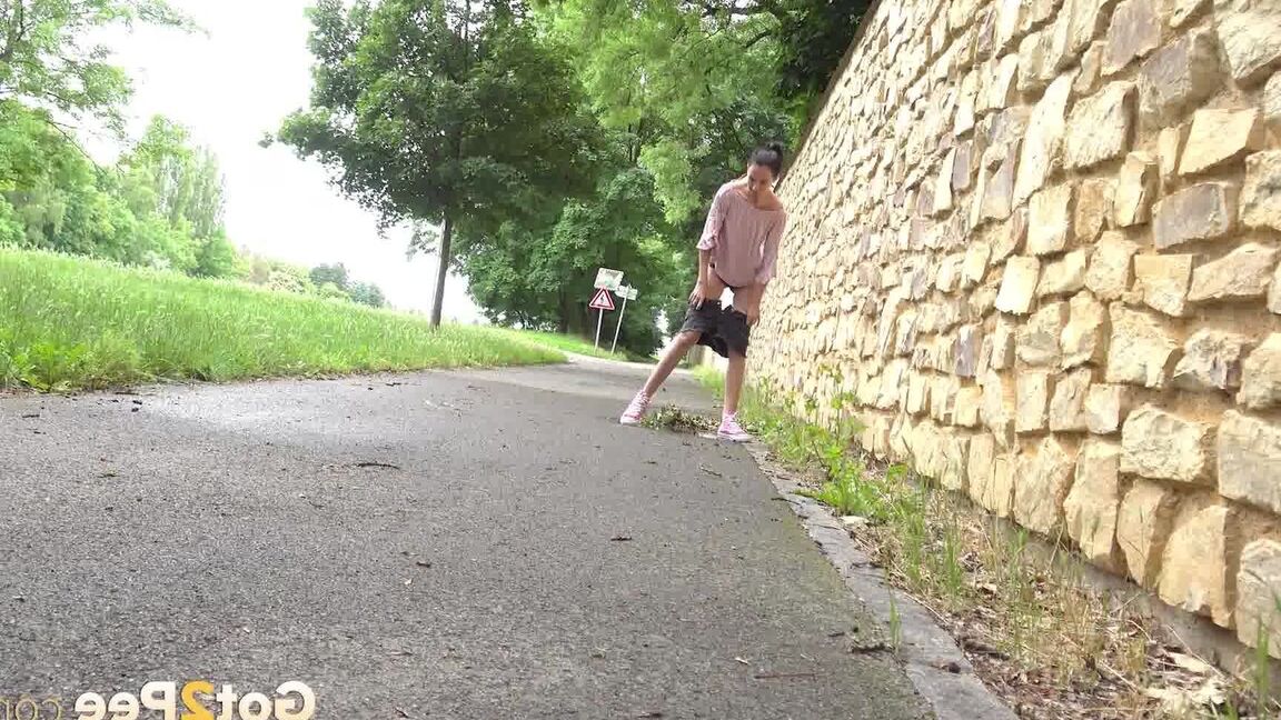 15P Short taken girl Mistica squats for a piss on a paved path in an urban setting