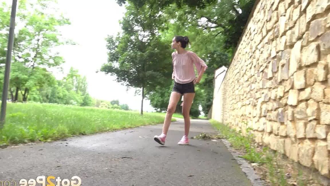15P Short taken girl Mistica squats for a piss on a paved path in an urban setting