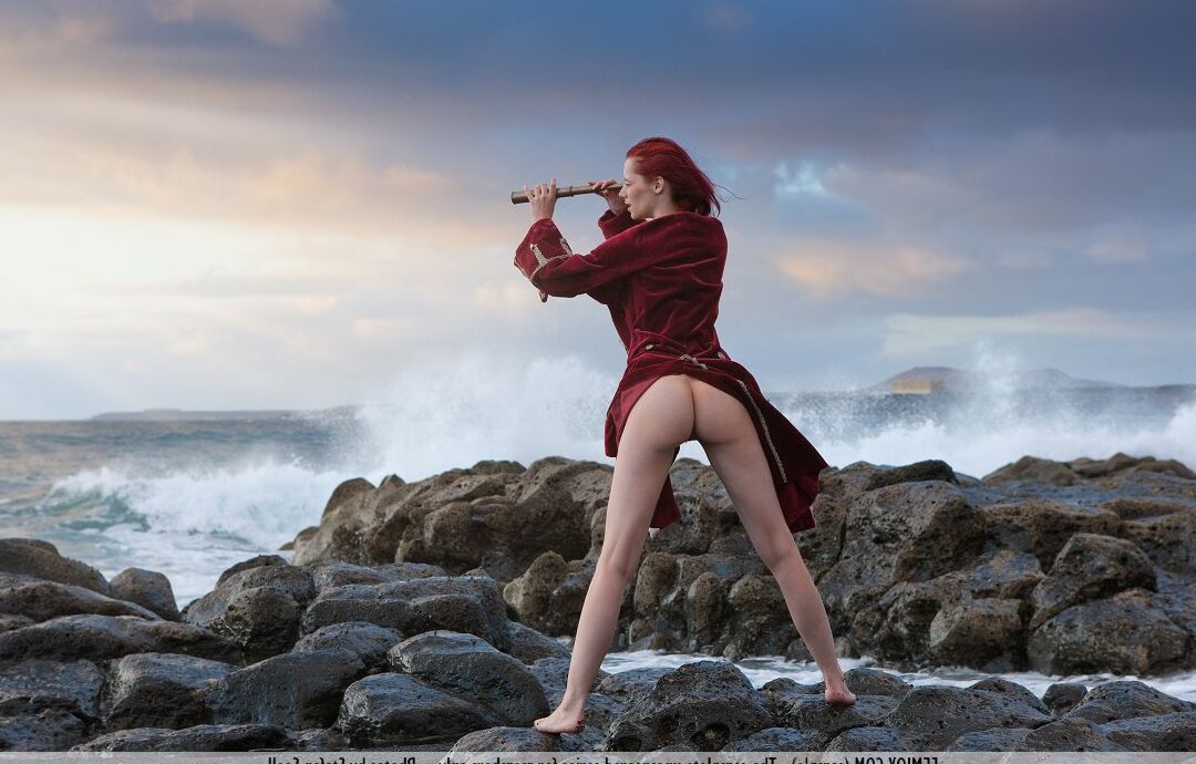 16P Busty redhead Ariel looks through a spyglass while naked at the ocean