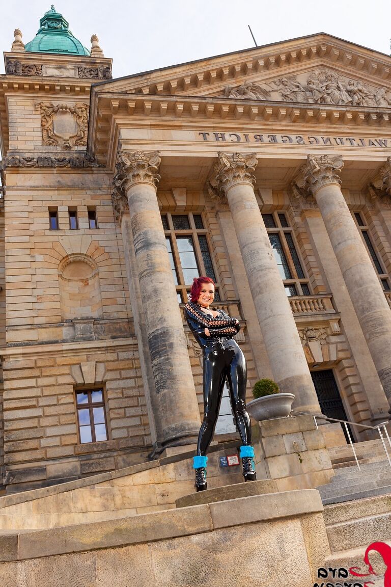 12P Redhead model Lara Larsen stands in a public square with attired in latex