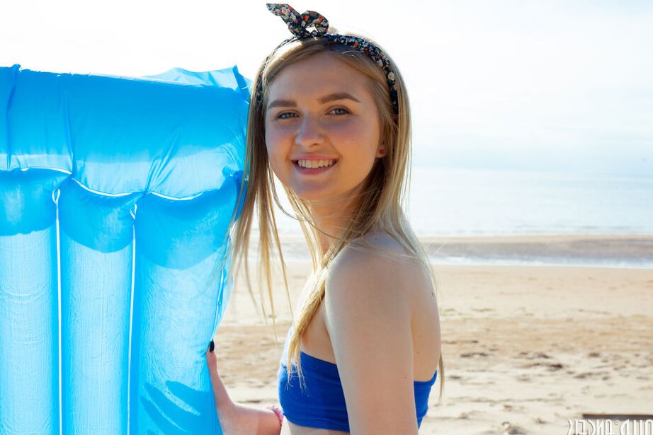 20P Die junge blonde Nimfa zieht am Strand ihre Shorts aus, um sich nackt in der Sonne auszubreiten