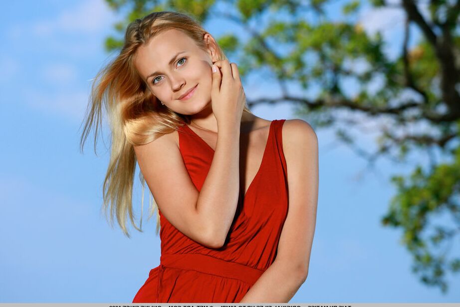 Der 17-jährige blonde russische Teenager Tais schlüpft aus einem roten Kleid, um nackt am Meer zu modeln