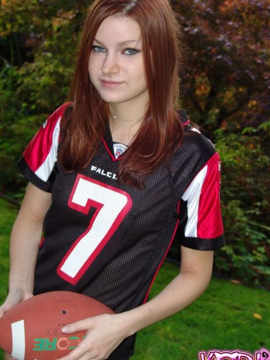 12P Korina Bliss, rousse naturelle, couvre ses seins exposés tout en tenant un ballon de football