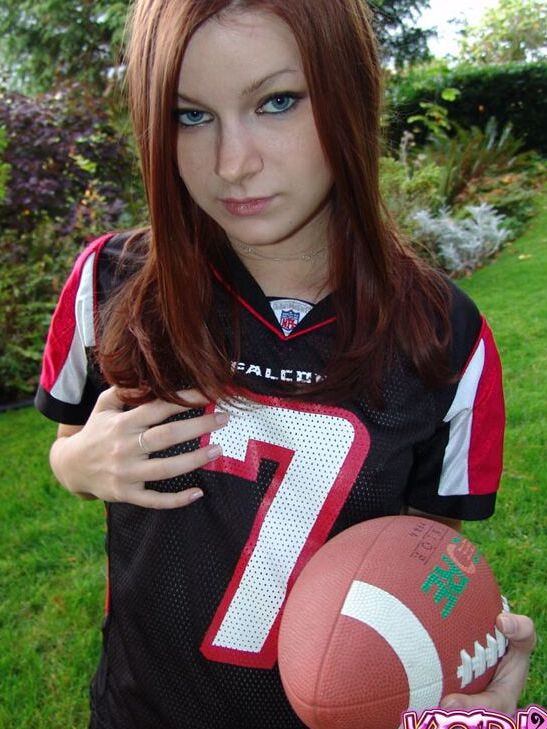 12P Korina Bliss, rousse naturelle, couvre ses seins exposés tout en tenant un ballon de football