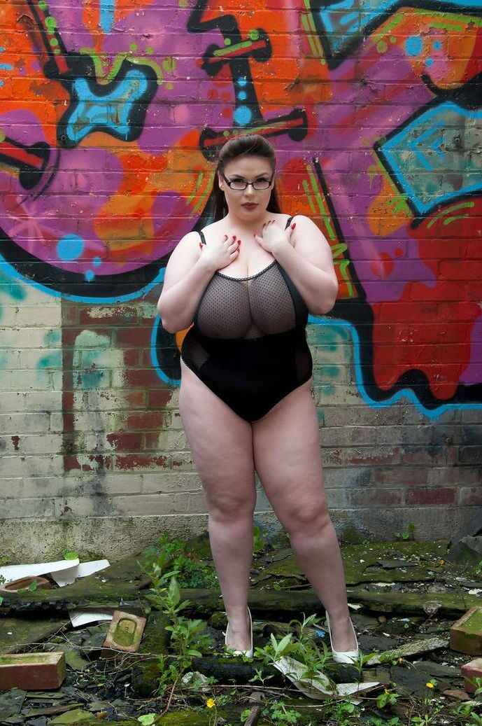 15P Brunette fatty Gina G unleashes her knockers while getting naked near graffiti