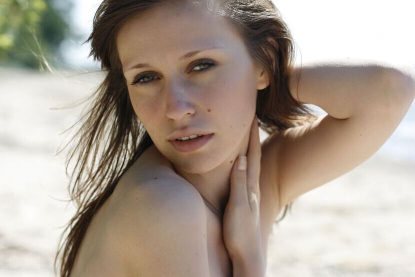 16P, Lilly B, une fille caucasienne, montre ses petits seins et sa chatte sur une plage de sable.