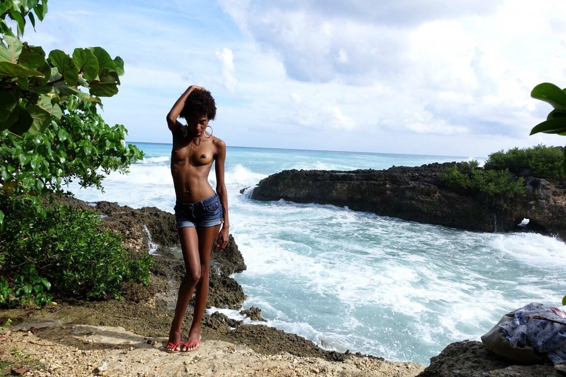 16P In front of the waves crashing on the rocks, a beautiful young black girl is