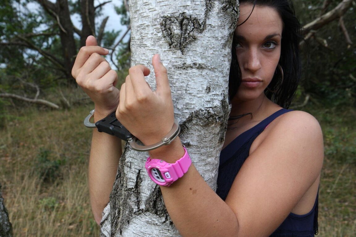 16P Брюнетка Нора прикована наручниками к дереву и носит розовые часы G-Shock.