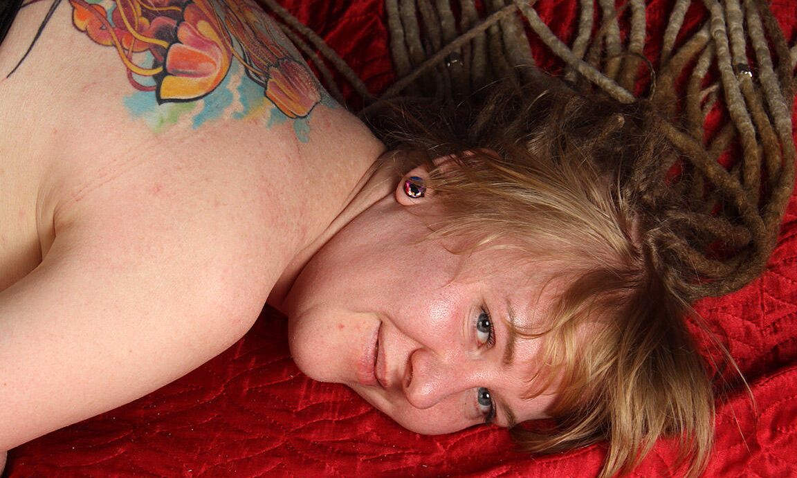 16P Tätowierte Frau trägt langes Haar, während ihre Handgelenke und Knöchel zusammengebunden sind