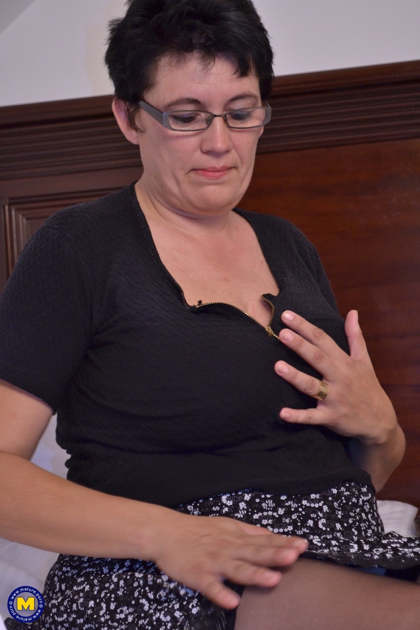 21P Short haired aunty in glasses Charlotte rubs and toys her clam on a bed
