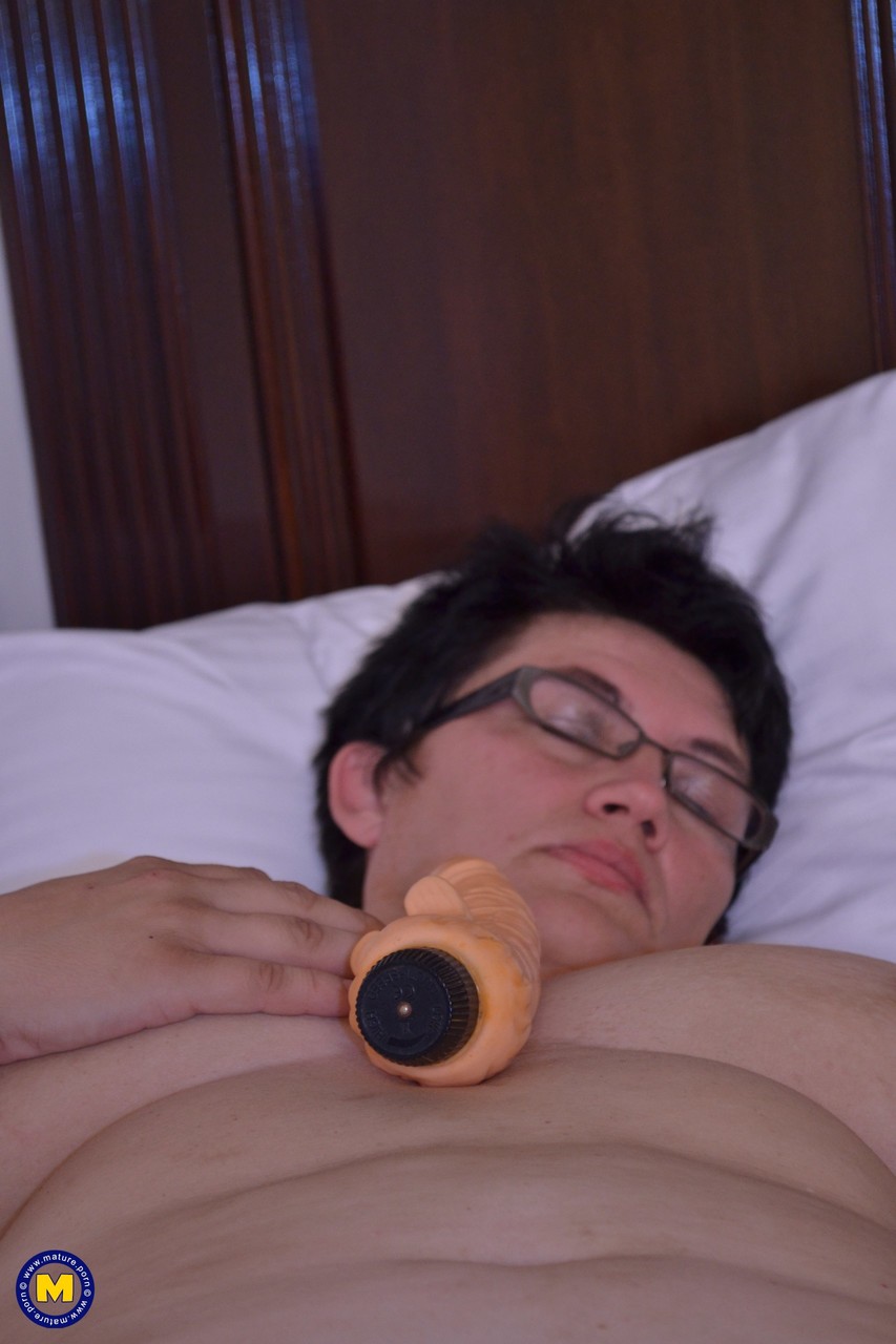 21P Short haired aunty in glasses Charlotte rubs and toys her clam on a bed
