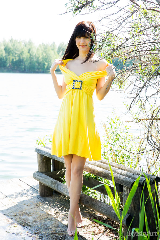 16P Uma jovem morena com um vestido amarelo mostra suas partes femininas à beira de um rio