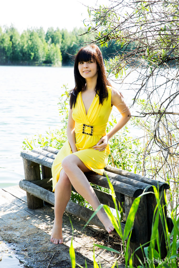 16P Uma jovem morena com um vestido amarelo mostra suas partes femininas à beira de um rio