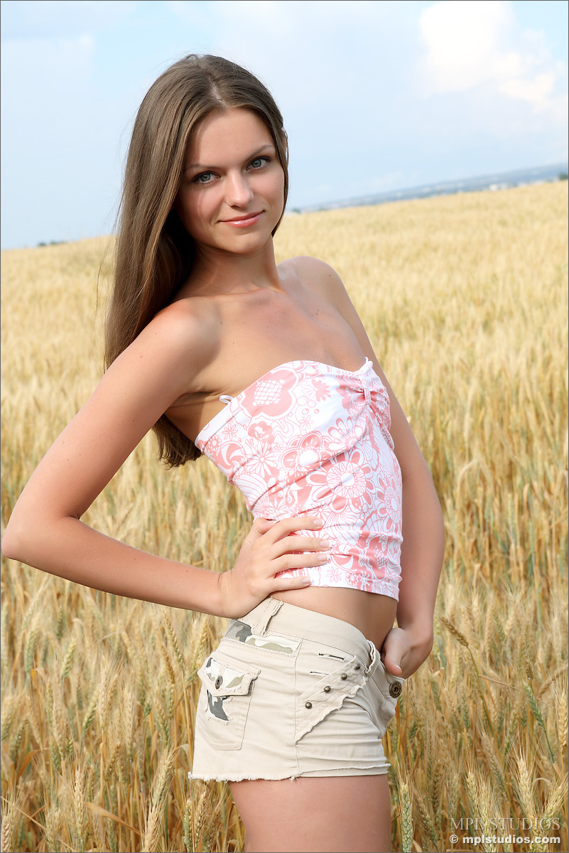 12P Solo girl twists her hair while standing naked in a field of wheat