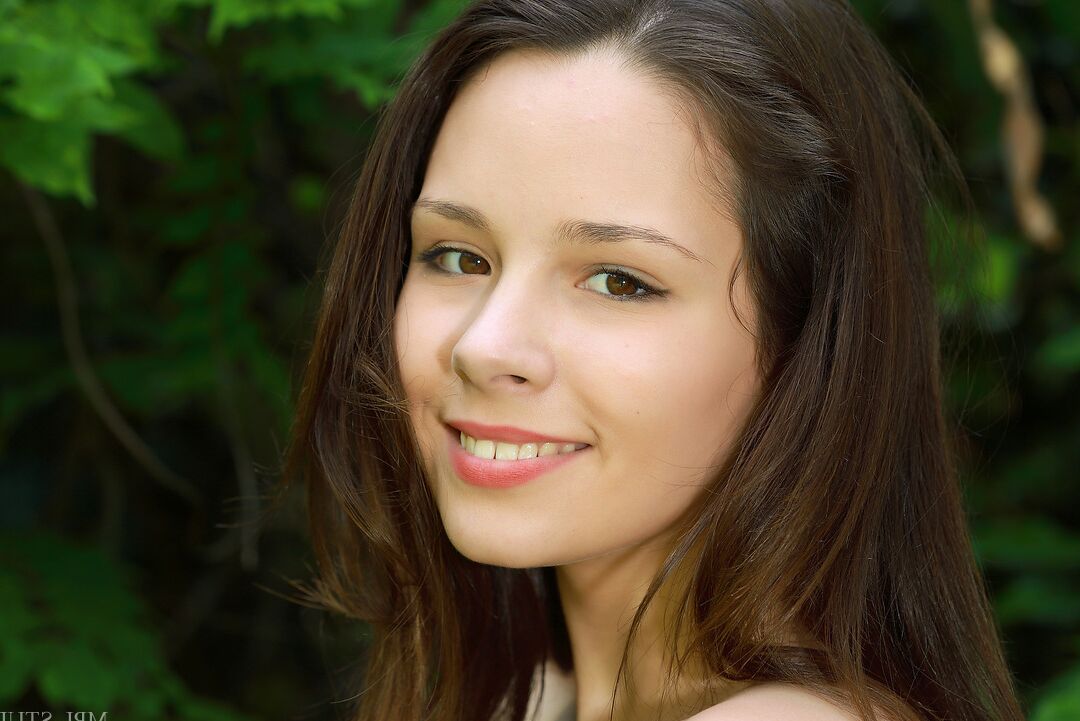 12P Charming young girl with a pretty face models bare naked near trees