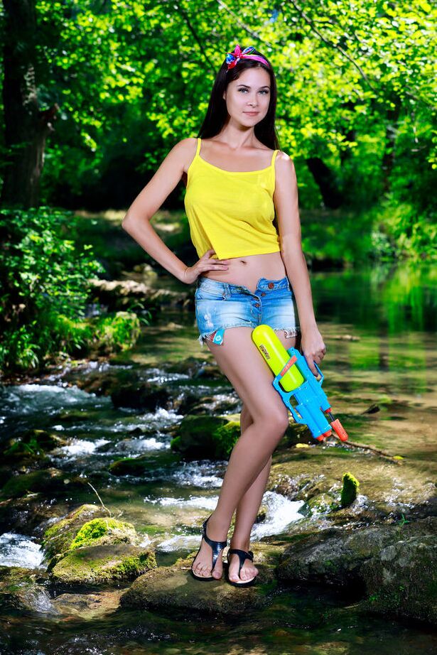 18P Young brunette Martina Mink wields a water gun while getting naked by a brook