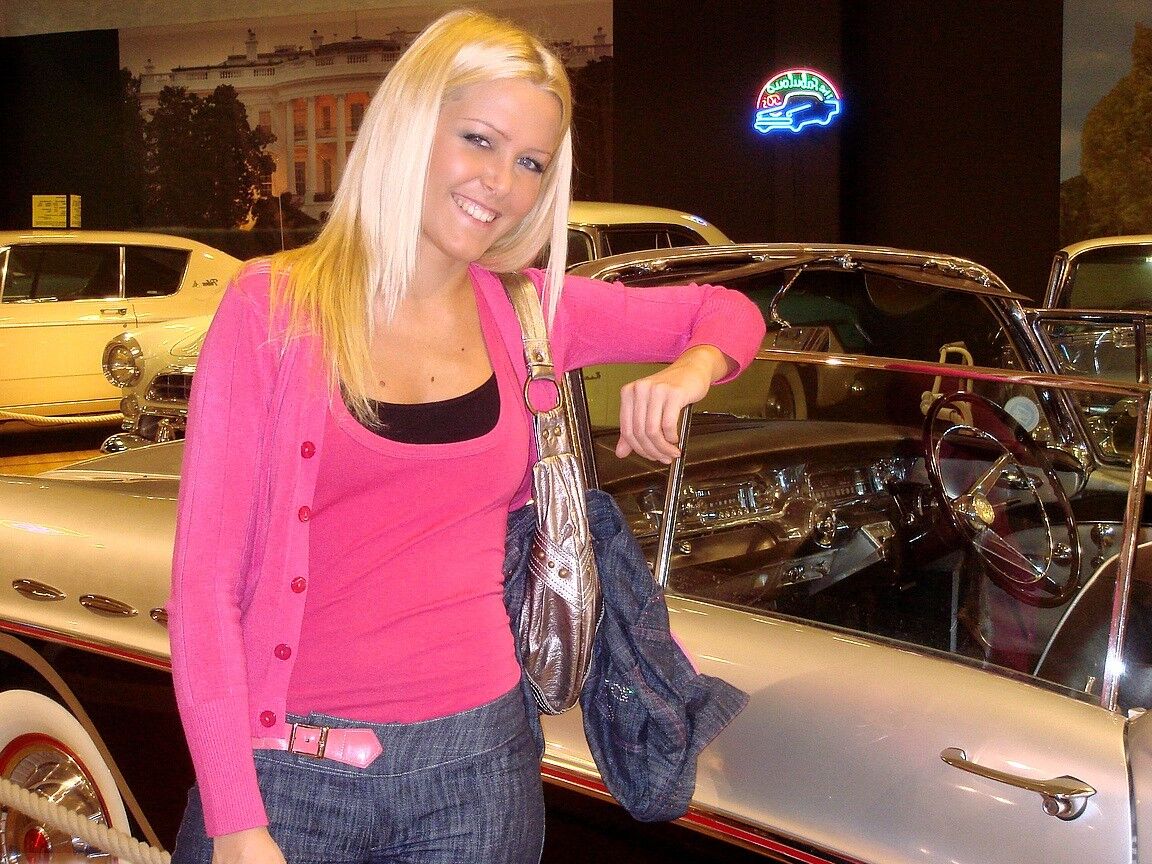 17P Sophie Moone, une MILF blonde hongroise, pose entièrement habillée devant des voitures.