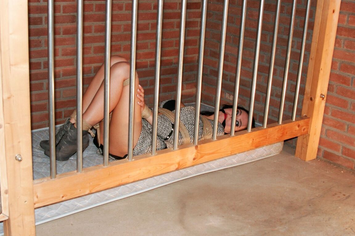 17P Une brune vêtue est laissée sur un matelas derrière des barreaux, attachée avec une corde et bâillonnée.