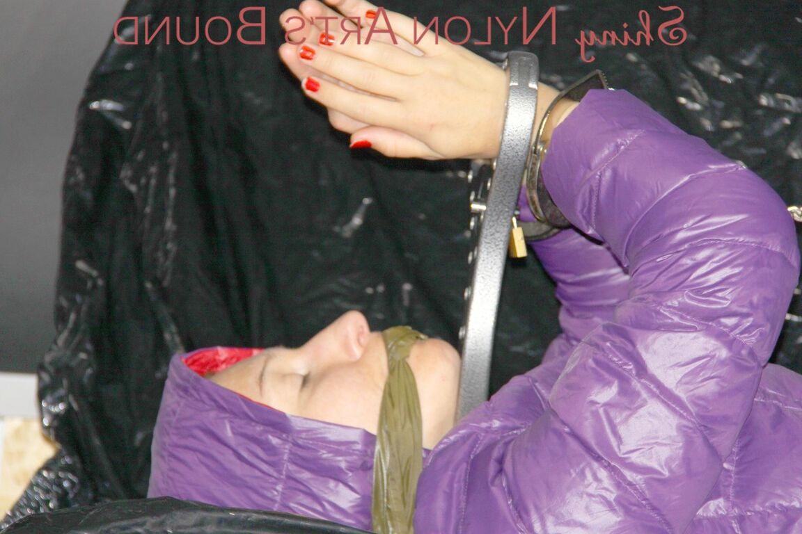 16P Sandra ist mit Handschellen und einem Pranger in heißem Lila auf einem Sofa gefesselt und geknebelt