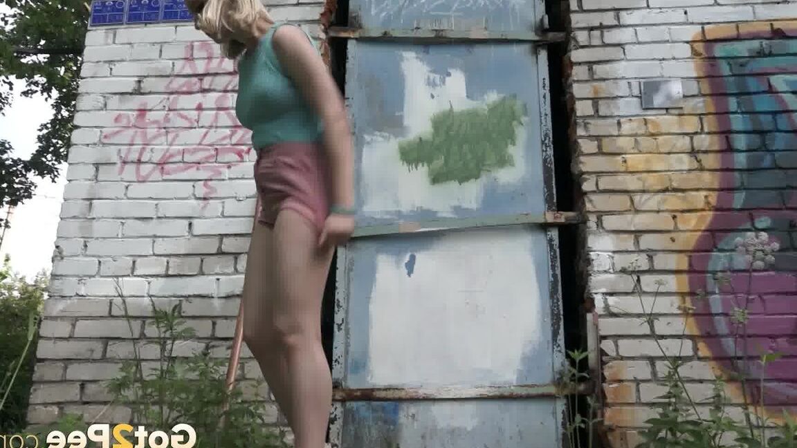 15P Blonde girl Masha squats for a pee on a concrete slab afore a barred door