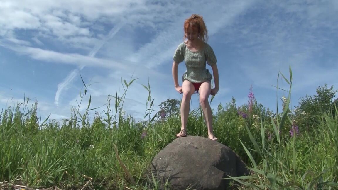 15P Redhead babe pees over a massive rock outside