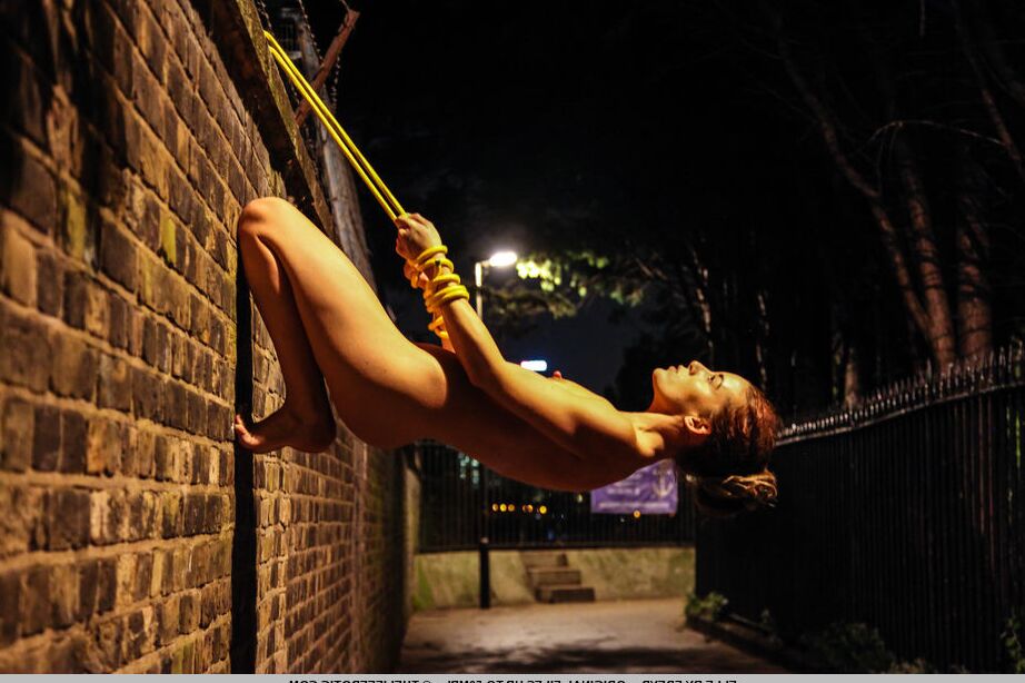 16P Une adolescente nue est attachée à un mur de briques avec une corde jaune la nuit